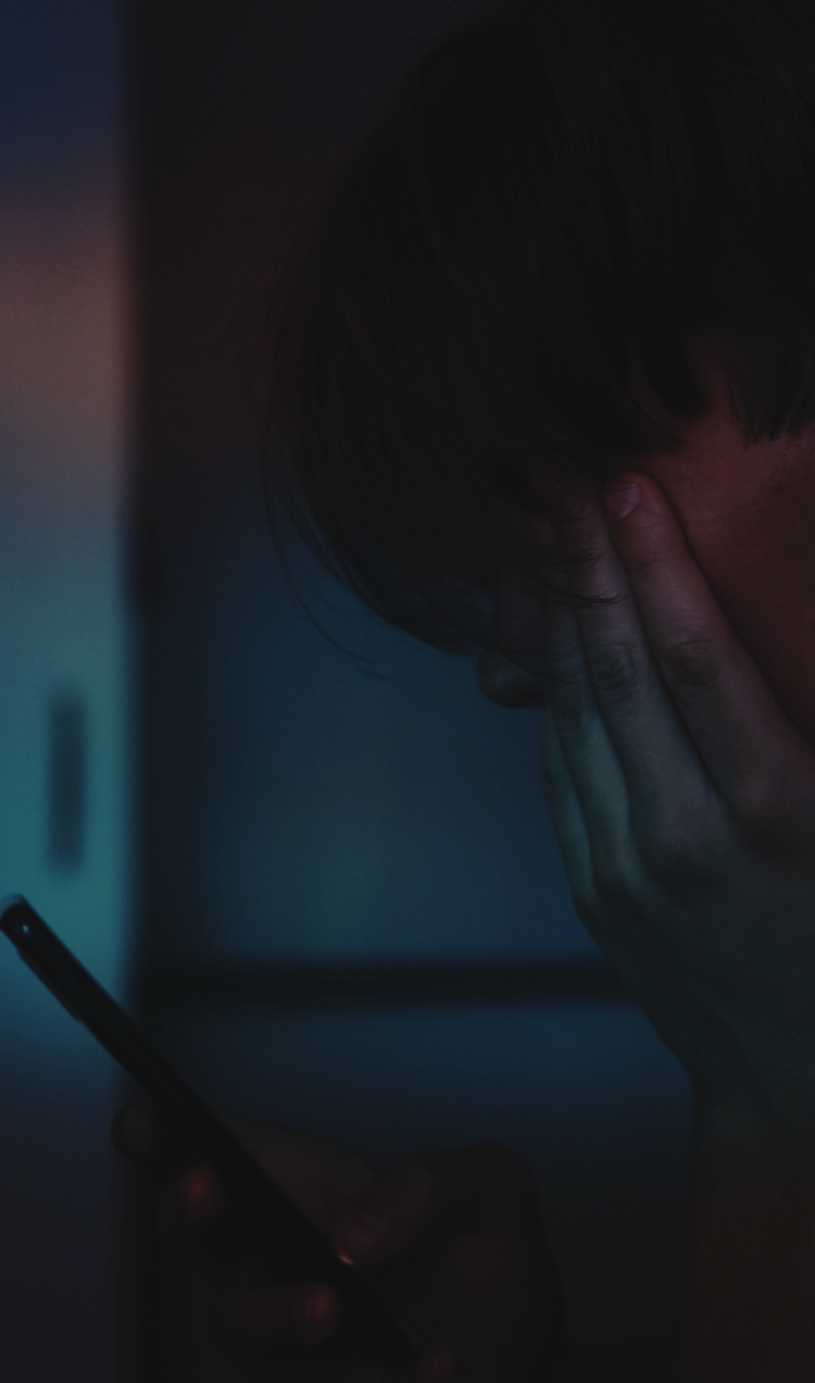 A person stares at their phone with their hand over their face.